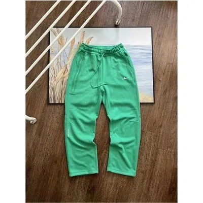 Green drawstring sweatpants hanging on a wooden hanger beside a framed print